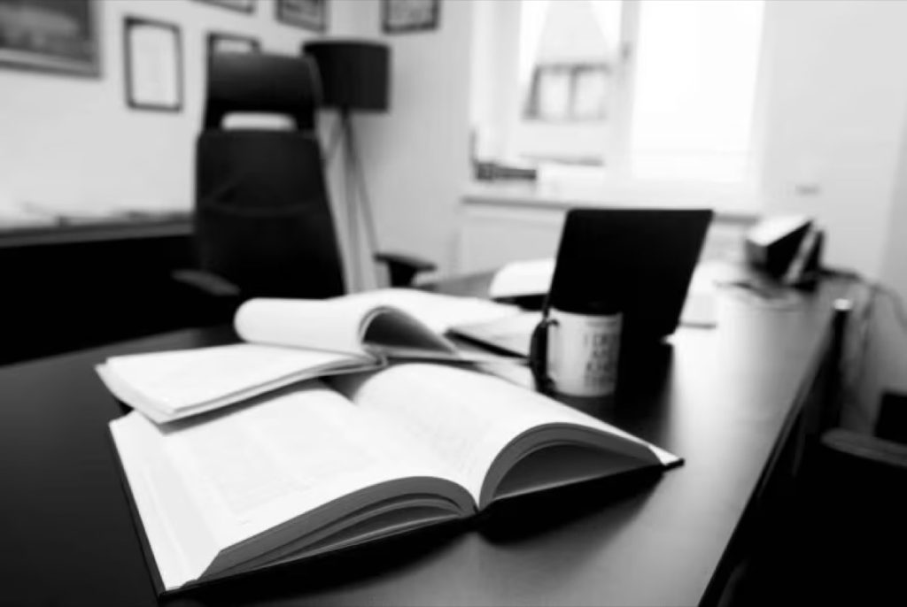 Open book and coffee mug on a dark office desk, in black and white