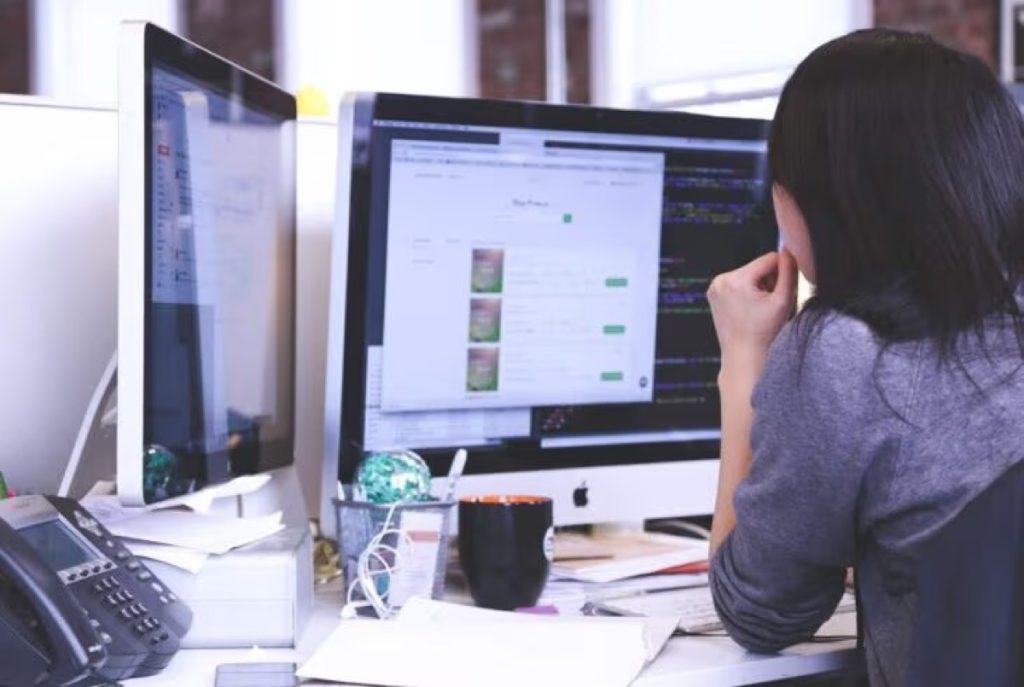 Woman looking at a website on a desktop monitor with code on a second screen