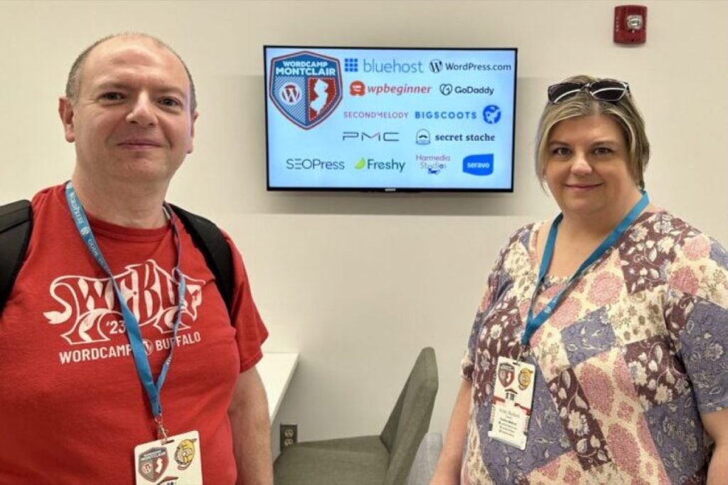 Chris and Kristy Basham at WordCamp Montclair 2024 in front of a sponsor display screen
