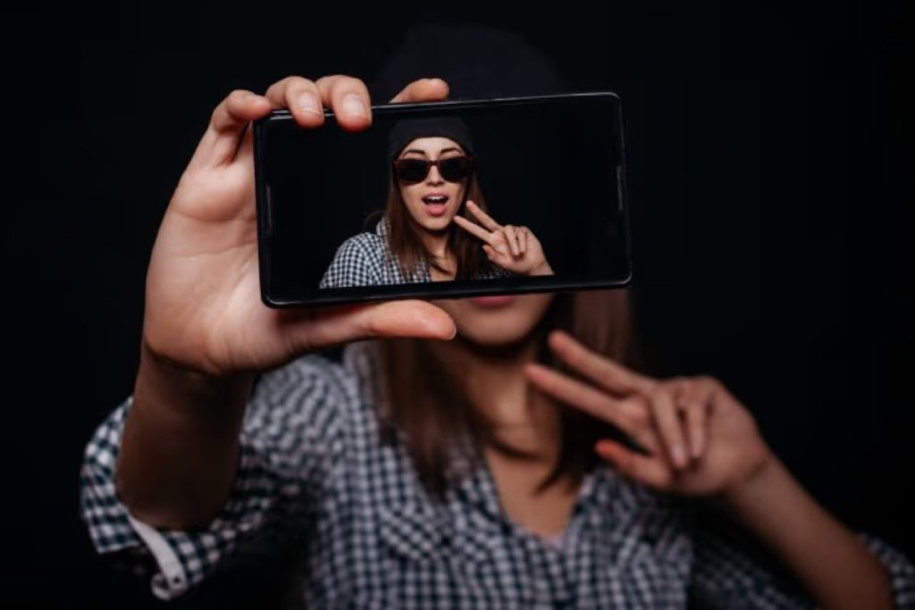 Woman holding up a phone that shows her in sunglasses making a peace sign